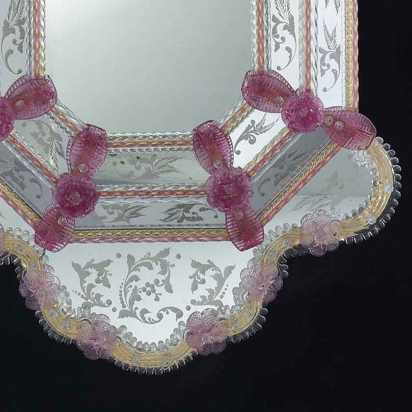 particolare decorativo di specchio veneziano in stile classico con fasce incise a mano e ricci, canne, foglie e fiori in vetro di murano di colore rosa e oro su fondo oro