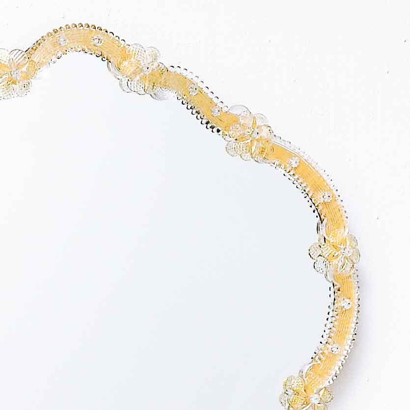 cornice di specchio veneziano con ricci e fiori in vetro di murano di colore cristallo su fondo oro.